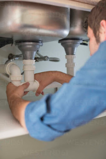 Plumber fitting waste pipework under a stainless steel sink